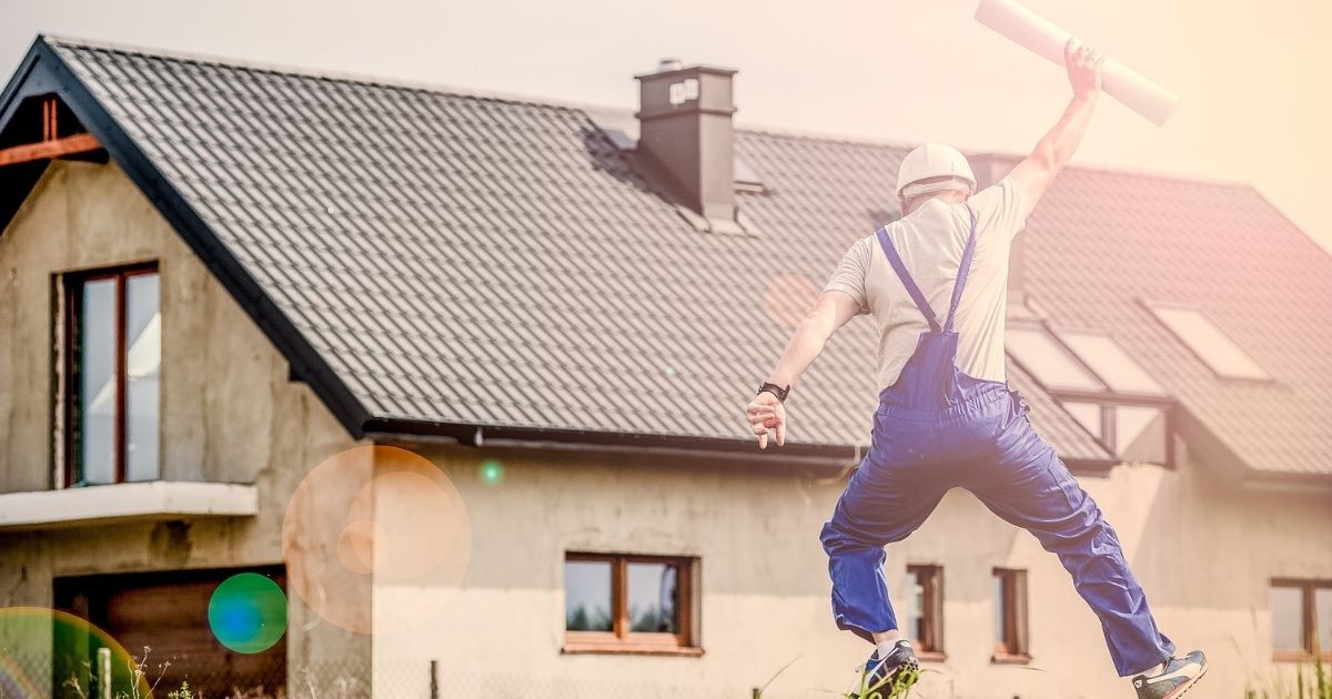 home builder tradesperson jumping for joy outside house with plans in hand